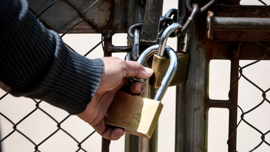 Una mano sostiene un candado semi abierto, en el portón de una cárcel